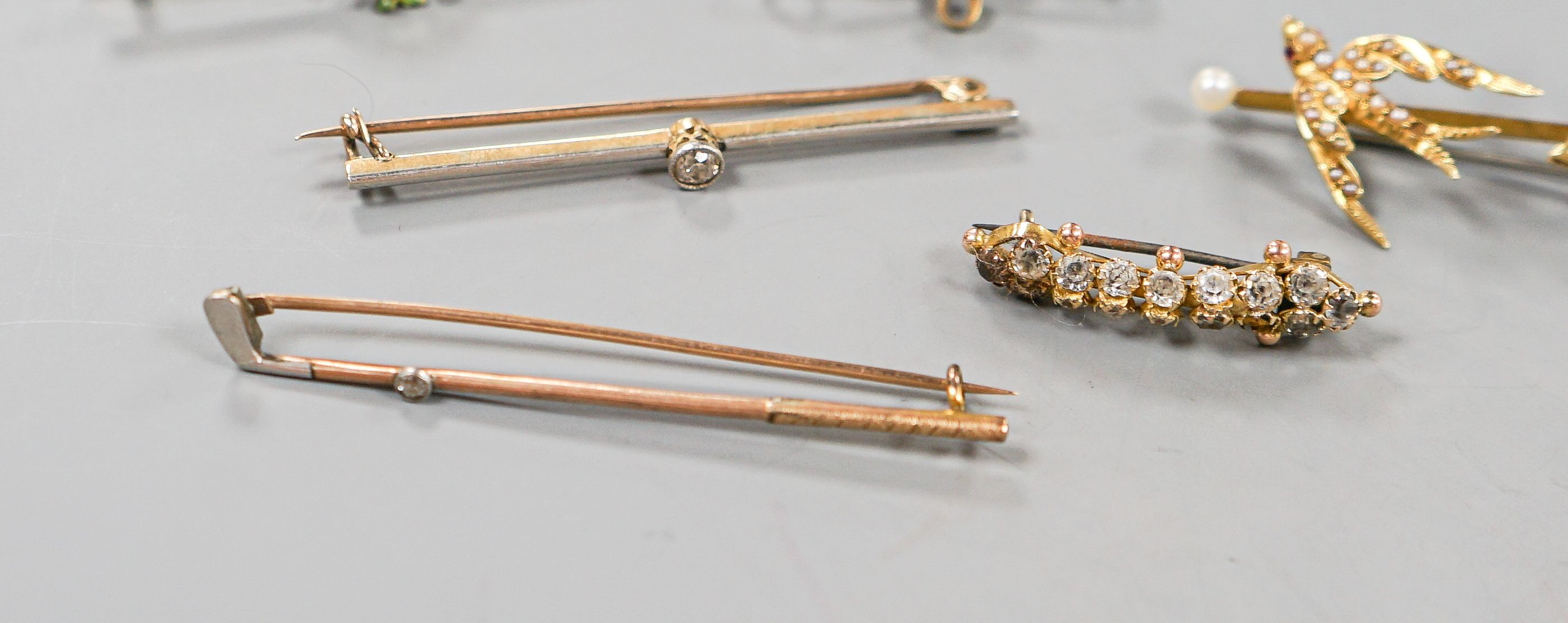A collection of six assorted yellow metal bar brooches, including seed pearl set twin swallow, diamond set gold club and solitaire diamond set